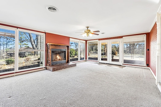 unfurnished living room with carpet, french doors, visible vents, ornamental molding, and a glass covered fireplace