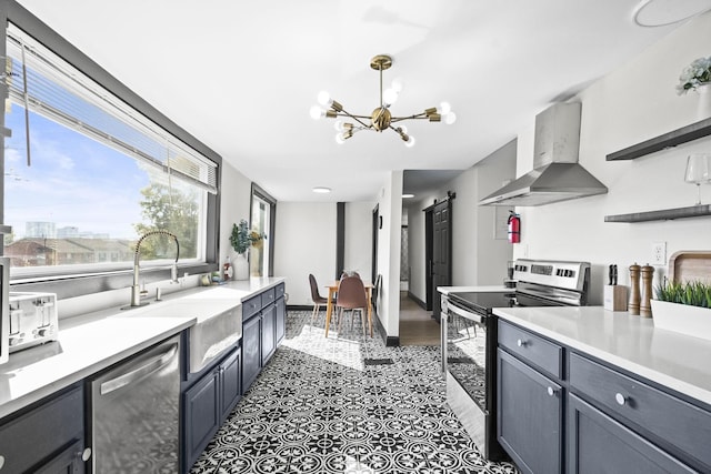 kitchen featuring wall chimney range hood, sink, stainless steel appliances, a notable chandelier, and a barn door