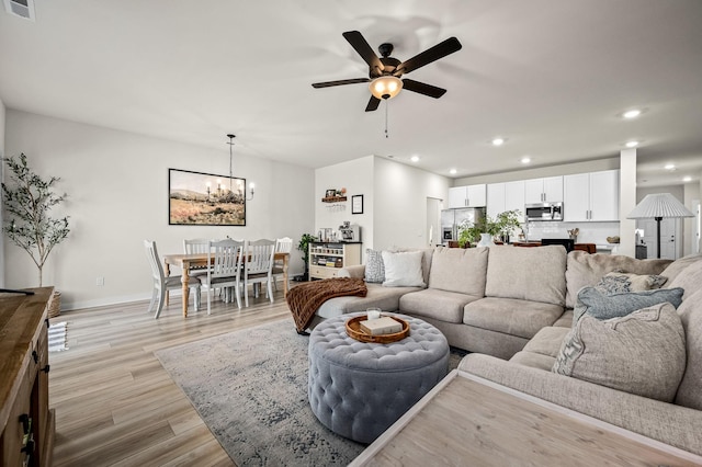 living room featuring ceiling fan with notable chandelier and light hardwood / wood-style flooring