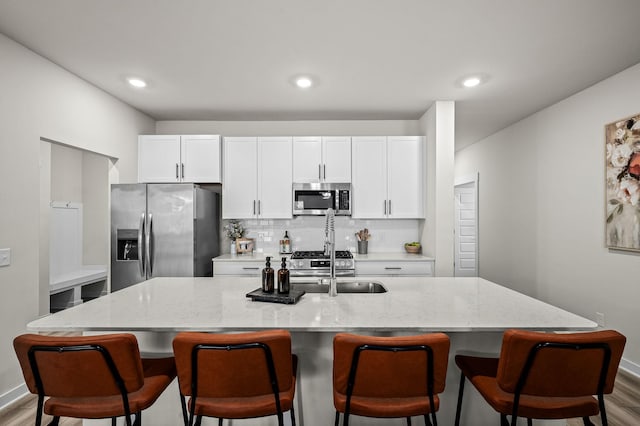 kitchen with light stone countertops, appliances with stainless steel finishes, a center island with sink, and white cabinets