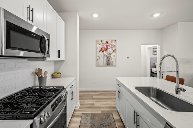 kitchen with stainless steel appliances, sink, white cabinets, and light stone counters