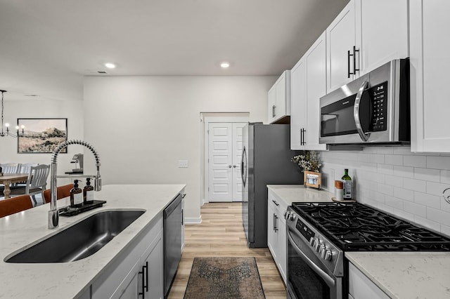 kitchen featuring pendant lighting, sink, stainless steel appliances, light stone counters, and white cabinets