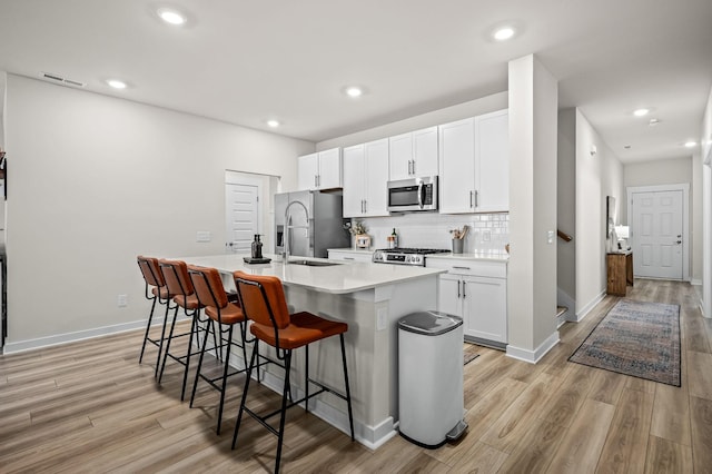 kitchen with sink, a breakfast bar area, stainless steel appliances, white cabinets, and a center island with sink