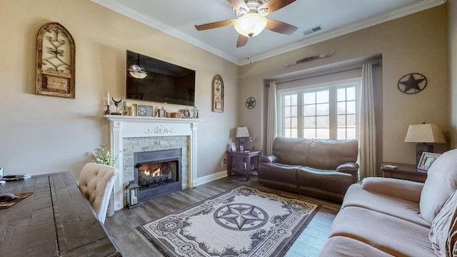 living area featuring a warm lit fireplace, visible vents, a ceiling fan, wood finished floors, and crown molding