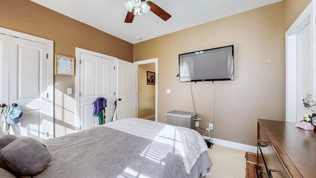 carpeted bedroom with two closets, baseboards, and a ceiling fan