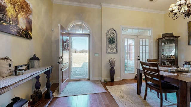 entryway with ornamental molding, a wealth of natural light, a notable chandelier, and wood finished floors