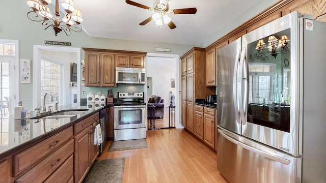 kitchen featuring brown cabinetry, dark stone countertops, stainless steel appliances, light wood-style floors, and a sink