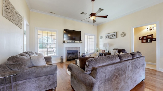 living room featuring crown molding, a ceiling fan, wood finished floors, a tile fireplace, and baseboards