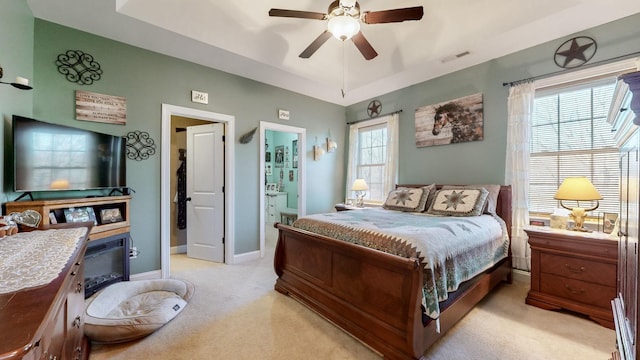 bedroom with connected bathroom, light carpet, visible vents, baseboards, and a tray ceiling