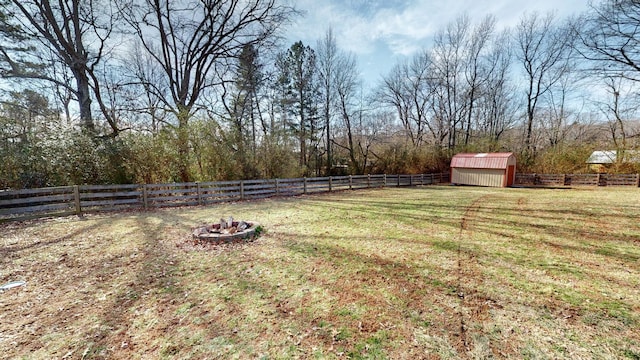 view of yard with an outbuilding, a rural view, a fenced backyard, a fire pit, and a shed