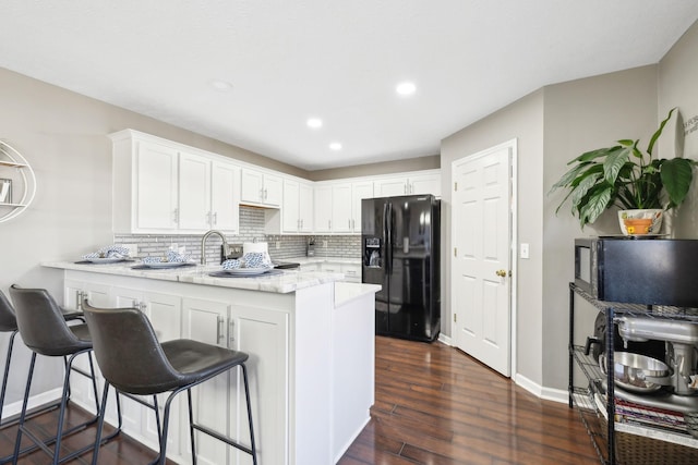 kitchen with a breakfast bar, white cabinets, black refrigerator with ice dispenser, and kitchen peninsula