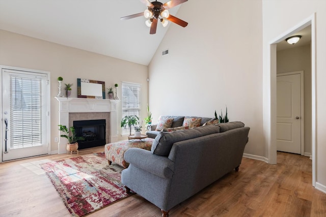 living room featuring hardwood / wood-style flooring, ceiling fan, a tiled fireplace, and high vaulted ceiling