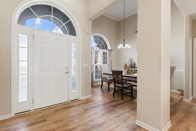 entrance foyer with a high ceiling, crown molding, an inviting chandelier, and light hardwood / wood-style flooring