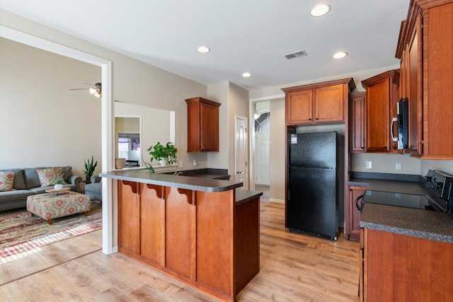 kitchen featuring stove, a kitchen breakfast bar, black fridge, kitchen peninsula, and light wood-type flooring