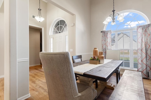 dining space featuring light hardwood / wood-style floors, a high ceiling, and a notable chandelier