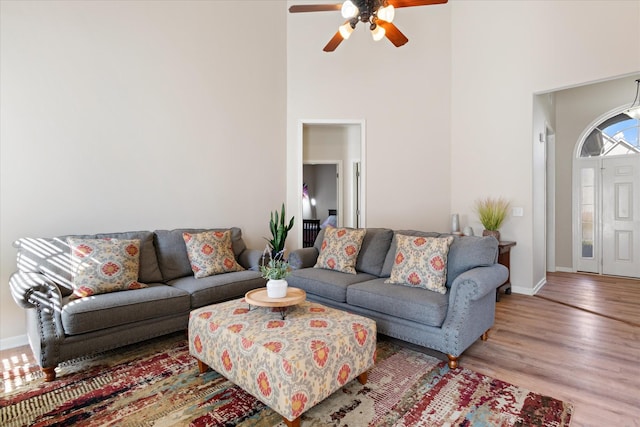 living room with a high ceiling, ceiling fan, and light hardwood / wood-style floors