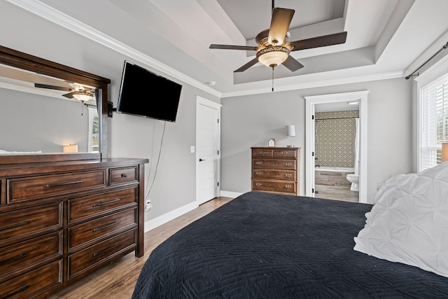 bedroom featuring ceiling fan, ensuite bath, a tray ceiling, and light wood-type flooring