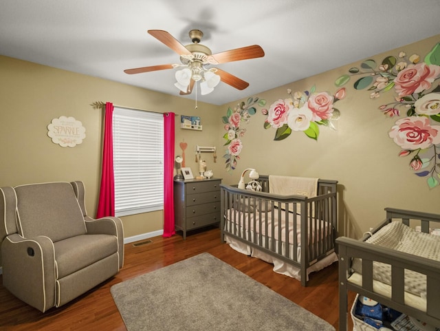 bedroom featuring a nursery area, ceiling fan, and dark hardwood / wood-style floors