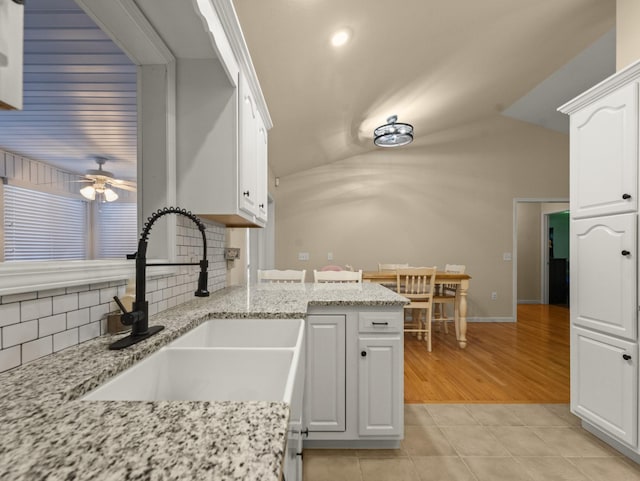 kitchen with light stone counters, kitchen peninsula, sink, and white cabinets