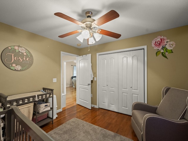 bedroom featuring a crib, dark hardwood / wood-style flooring, ceiling fan, and a closet