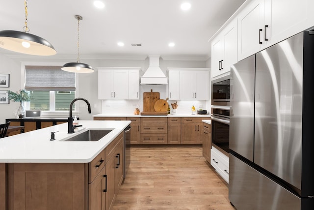 kitchen with premium range hood, an island with sink, white cabinetry, sink, and stainless steel appliances