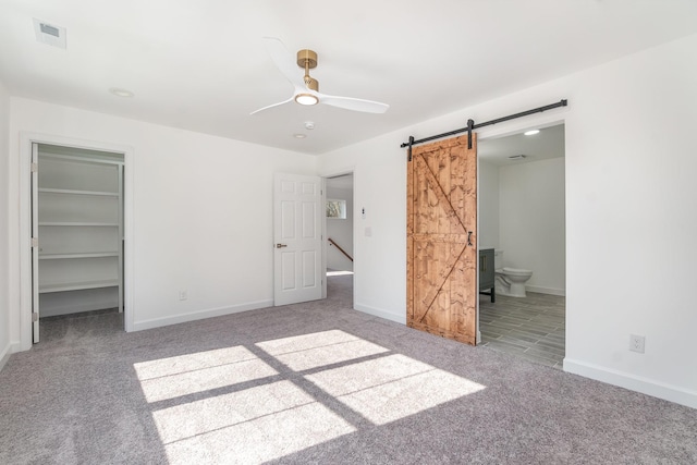 unfurnished bedroom featuring ensuite bath, a walk in closet, a barn door, and carpet