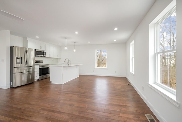 kitchen featuring appliances with stainless steel finishes, pendant lighting, white cabinetry, a kitchen island with sink, and dark wood-type flooring