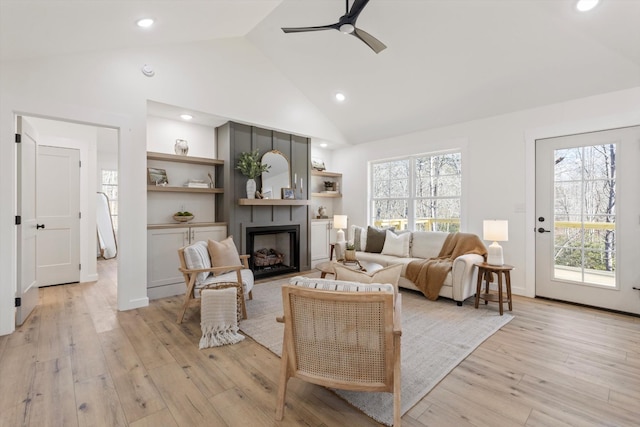 living room featuring a fireplace, light hardwood / wood-style flooring, high vaulted ceiling, and ceiling fan