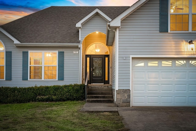 exterior entry at dusk featuring a yard and a garage