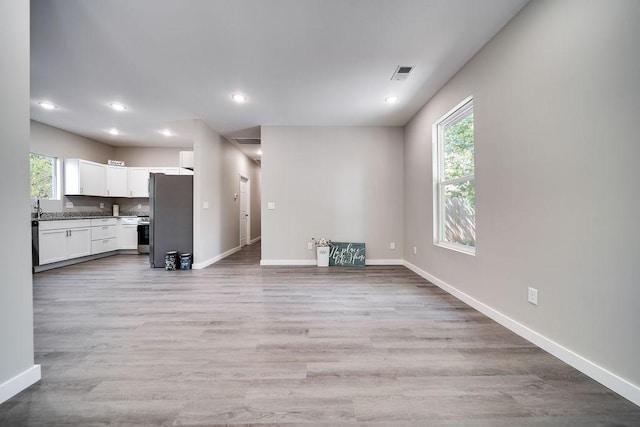 unfurnished living room featuring sink, a healthy amount of sunlight, and light wood-type flooring