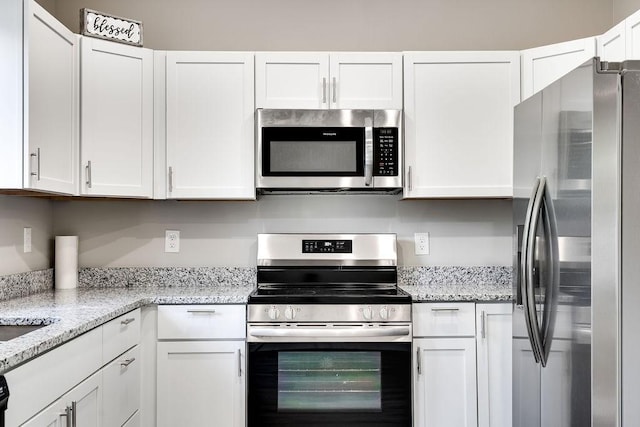 kitchen with stainless steel appliances, white cabinetry, and light stone countertops