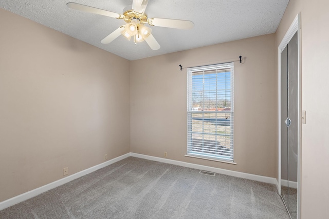 empty room with a healthy amount of sunlight, ceiling fan, a textured ceiling, and carpet