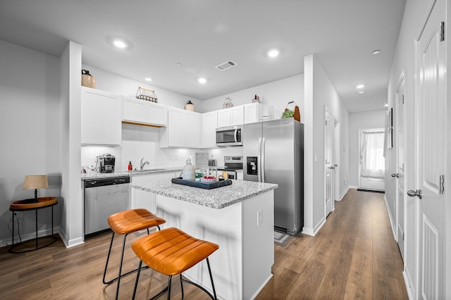 kitchen featuring white cabinetry, light stone counters, a center island, a kitchen breakfast bar, and stainless steel appliances