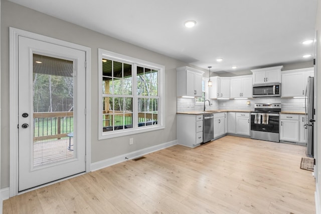 kitchen with tasteful backsplash, white cabinetry, sink, hanging light fixtures, and stainless steel appliances