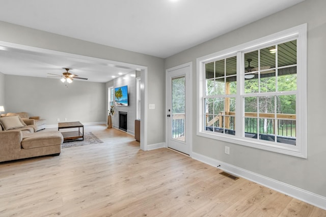 living room featuring ceiling fan, plenty of natural light, a large fireplace, and light wood-type flooring