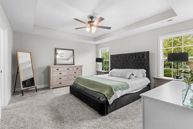 carpeted bedroom featuring a raised ceiling, ceiling fan, and multiple windows