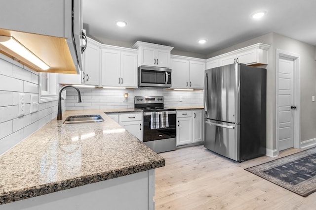 kitchen with sink, white cabinetry, light wood-type flooring, stainless steel appliances, and backsplash