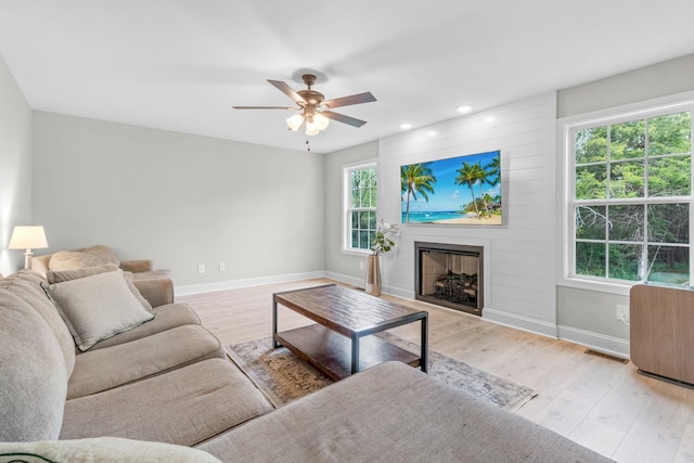 living room with ceiling fan, a large fireplace, and light hardwood / wood-style flooring