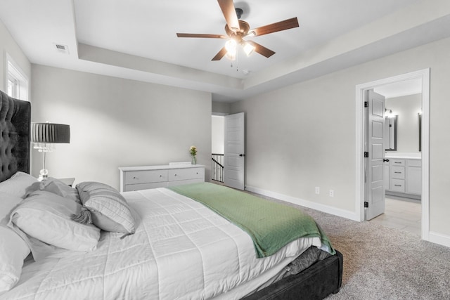 bedroom with light carpet, connected bathroom, a tray ceiling, and ceiling fan