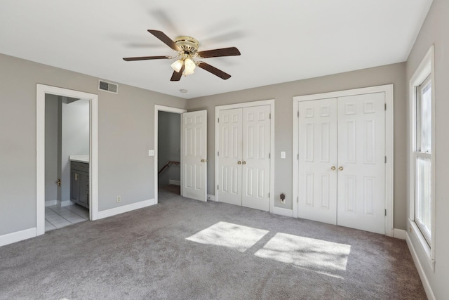 unfurnished bedroom with ceiling fan, ensuite bath, multiple closets, and light colored carpet