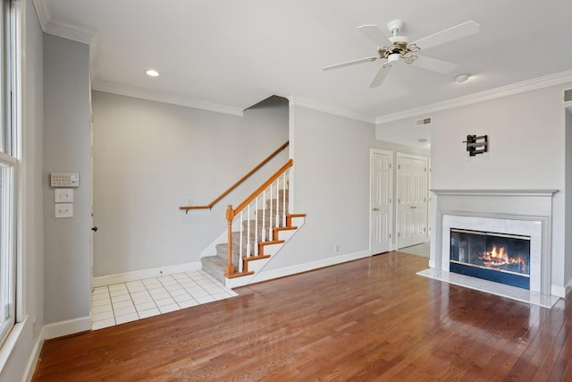 unfurnished living room with hardwood / wood-style floors, a high end fireplace, ornamental molding, and ceiling fan