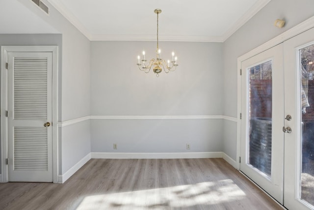 unfurnished dining area with crown molding, a notable chandelier, french doors, and light wood-type flooring