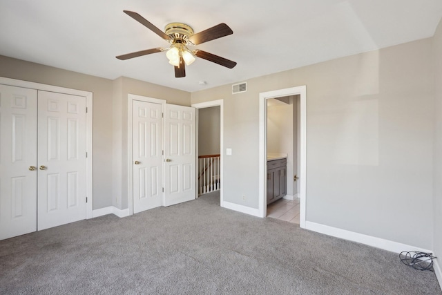 unfurnished bedroom with multiple closets, ceiling fan, ensuite bathroom, and light carpet