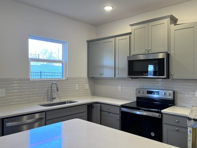 kitchen featuring gray cabinetry, appliances with stainless steel finishes, sink, and backsplash