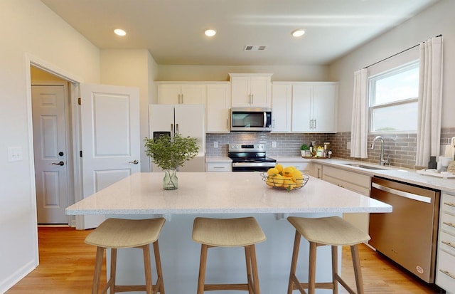 kitchen featuring stainless steel appliances, visible vents, decorative backsplash, a sink, and a kitchen bar