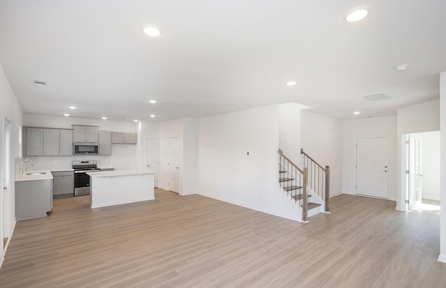 kitchen with light wood finished floors, stainless steel appliances, light countertops, gray cabinetry, and open floor plan