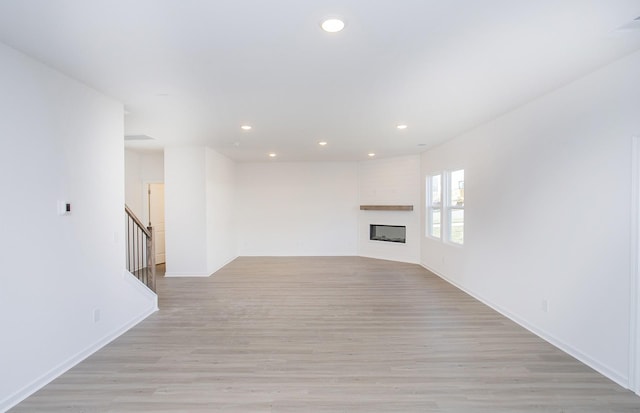 unfurnished living room with light wood-type flooring, stairs, a fireplace, and recessed lighting