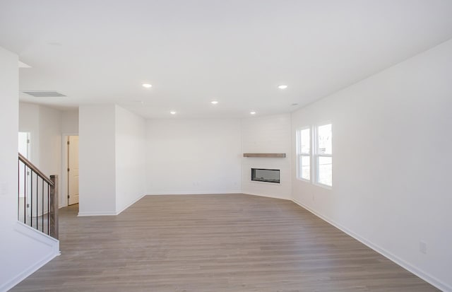 unfurnished living room featuring recessed lighting, wood finished floors, a fireplace, and stairs