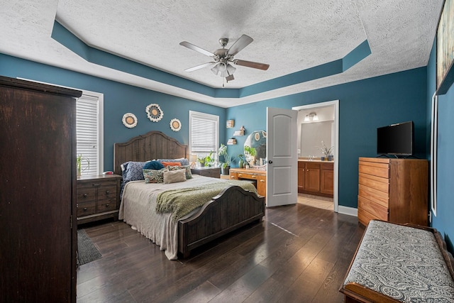 bedroom featuring a raised ceiling, dark hardwood / wood-style flooring, ceiling fan, and ensuite bath