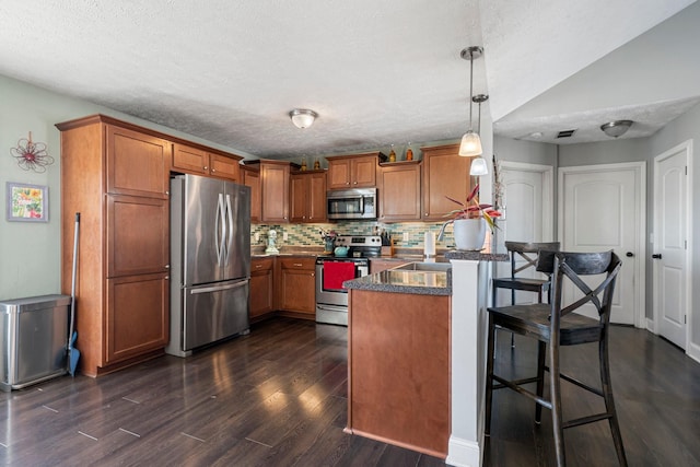 kitchen with stainless steel appliances, dark hardwood / wood-style floors, a kitchen breakfast bar, tasteful backsplash, and decorative light fixtures